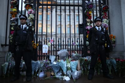 Blommor vid porten till Buckingham Palace. Två vakter står bredvid.