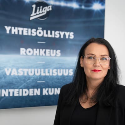 Kati Kivimäki taulun vieressä, jossa lukee SM-liigan arvot.