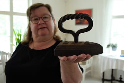 Kvinna håller i ett gammalt strykjärn med skruvat handtag.