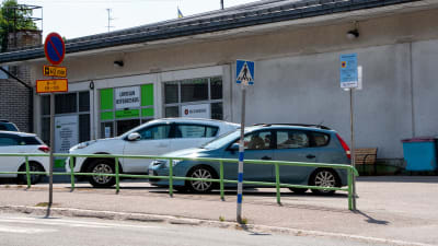 Bilar parkerade utanför en affärslokal. En skylt visar att området har parkeringsövervakning.