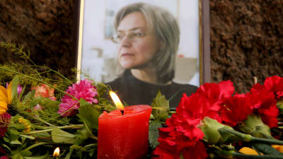 En bild på Anna Politkovskaya. I förgrunden syns blommor vid ett minnesmärke.