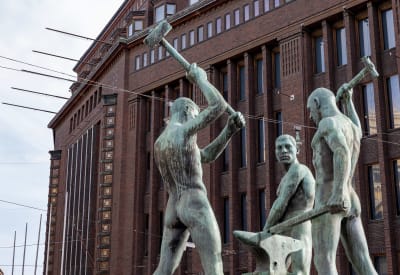 Statyn Tre smeder och i bakgrunden Stockmanns varuhus i Helsingfors centrum.