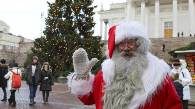 Julgubben vinkar framför en stor julgran och domkyrkan i Helsingfors.