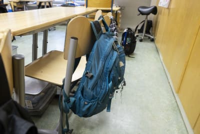 En skolväska hänger över en stolsrygg i ett klassrum.