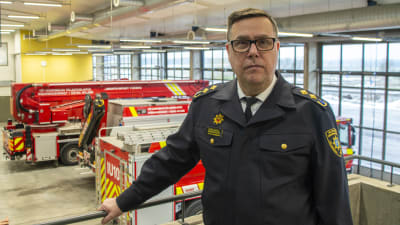 En person i räddningsverkets uniform står på en avsats i en brandstation. Bakom honom syns några räddningsfordon.