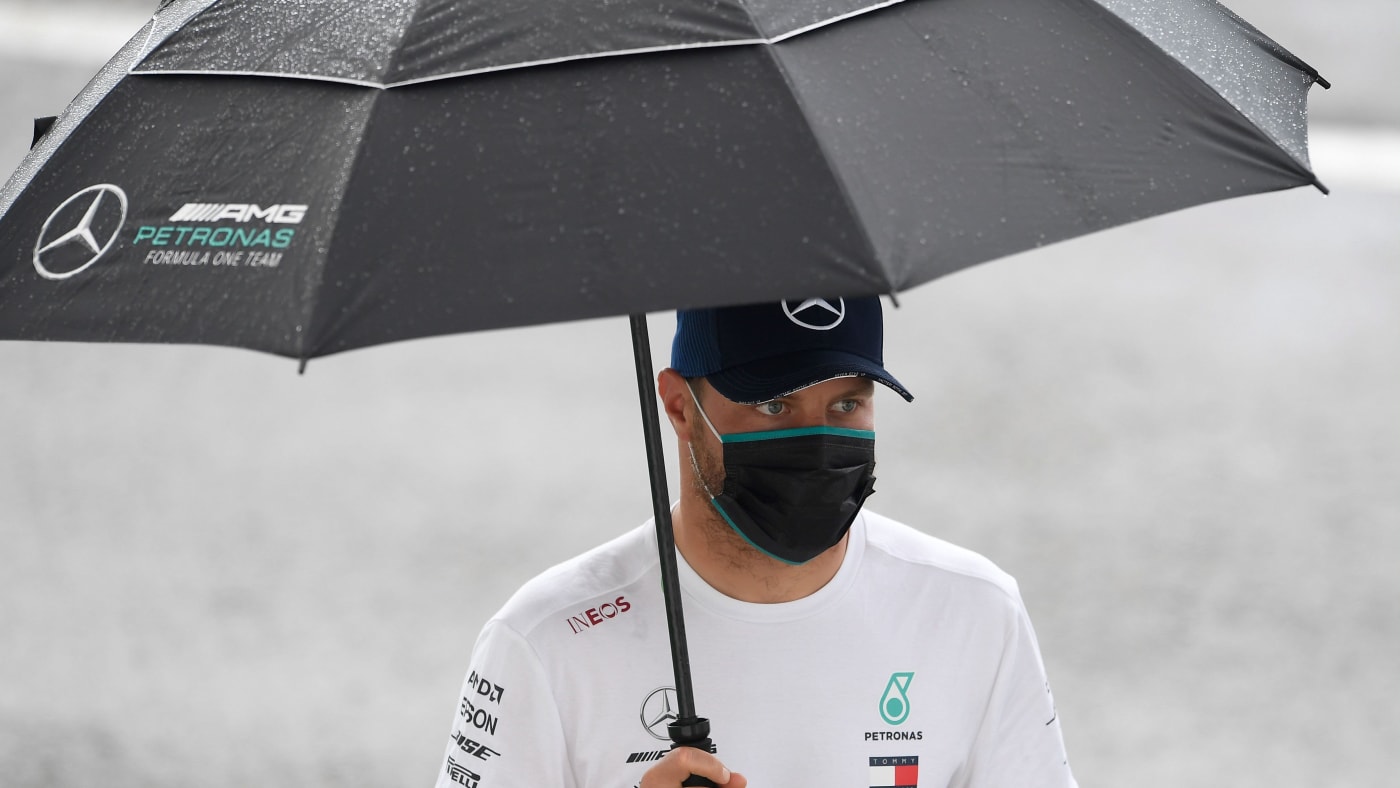 Valtteri Bottas walks in the rain with an umbrella.