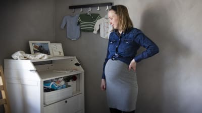 Sandra Holmgård är gravid i sjunde månaden och står framför en byrå med babykläder. 