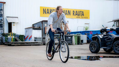 En man cyklar på en asfalterad gård, runt omkring ser man diverse tunnor och containrar.