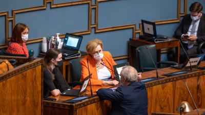 Antti RInne står med ryggen mot kameran och diskuterar med Sanna Marin och Tuula Haatainen i riksdagen under plenum 14.5.2021. 
