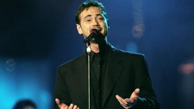 Christer Björkman sjunger i en mikrofon iklädd svart kostym år 1992