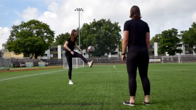 Två unga kvinnor står och sparkar fotboll på en konstgräsplan.