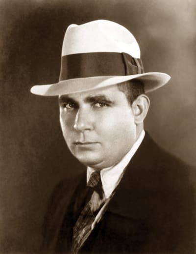 En ung man i svart kostym och vit hatt. 