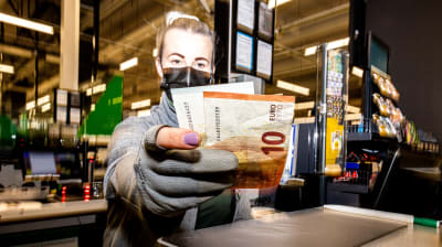 En försäljare vid en butikskassa sträcker fram pengar. 
