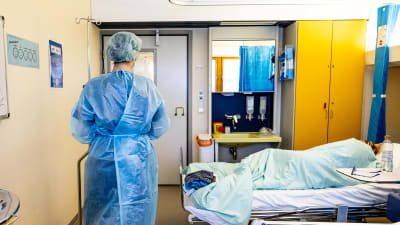 Suojavarusteisiin pukeutunut lähihoitaja Janina Kinnunen koronapotilaan kanssa.
