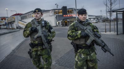 Två tungt beväpnade svenska soldater patrullerar utanför en hamnterminal. 