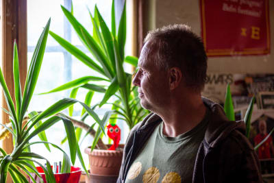 En man ser ut genom fönstret. I bakgrunden står det krukväxter.