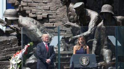 USA:s president Donald Trump står på scenen i Warszawa tillsammans med sin fru Melania. I bakgrunden statyer på soldater.