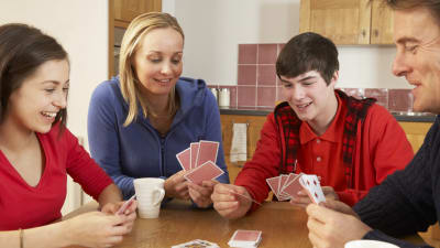 En familj med två tonårsbarn sitter runt ett bord och spelar kortspel