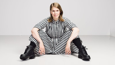 Toimittaja Julia Thurén istuu lattialla raidallisessa mekossa. 