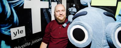 Jarkko Ryynänen poseeraa Voitto-uutisrobottia esittävän pehmolelun kanssa.