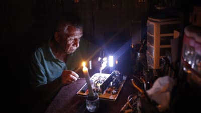 En man reparerar elektrisk apparatur i skenet av ett stearinljus i San Christobal, Venezuela 26.4.2016