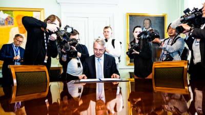 Utrikesminister Pekka Haavisto (Gröna) undertecknade Finlands Natoansökan. Bakom honom står många fotografer som förevigar händelsen.