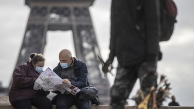 Två personer iklädda munskydd sitter och tittar på en karta. I bakgrunden ser man en del av Eiffeltornet.