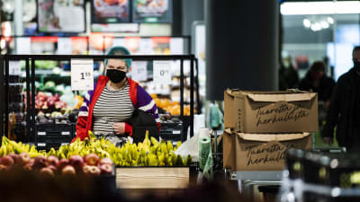 En kvinna står och tittar på prislappen på bananer i en större matbutiks frukt och grönt-avdelning.