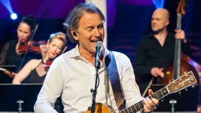 Tomas Ledin sjunger och spelar gitarr. Stråkmusiker i bakgrunden. 
