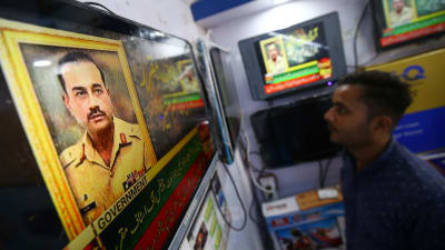 En man i Karachi ser på en tv-skärm med en bild av Pakistans nya arméchef, generallöjtnant Syed Asim Munir.