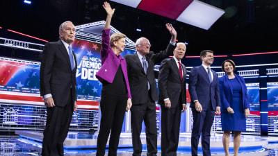 De demokratiska kandidaterna, fyra män i kostym, en kvinna i byxdress och en i blå klänning, står i en tv-studio.