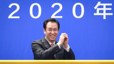 Affärsmannen Xu Jiayin iklädd kostym håller händerna i vädret. I bakgrunden siffrorna 2020.