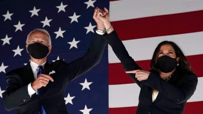 Kamala Harris står bredvid Joe Biden och håller upp hans hand. 