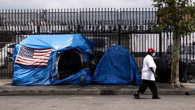 En kvinna iförd ansiktsskydd promenerar förbi ett blått tält prytt av en stor amerikansk flagga i Los Angeles den 20 april 2020.