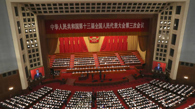 En bild av den kinesiska nationella folkkongressen fotad uppifrån. Man ser ledamöterna och en stor scen.