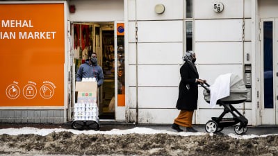 En kvinna i munskydd går med barnvagn i Helsingfors.