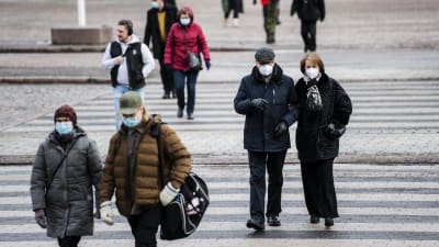 Människor i munskydd går i Helsingfors centrum i februari 2021.