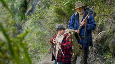 Poika (Julian Dennison) ja parrakas mies (Sam Neill) kiväärien kanssa mäkisessä maastossa. Kuva elokuvasta Hunt for the Wilderpeople.