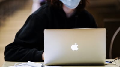 En person i munskydd sitter bakom en dator