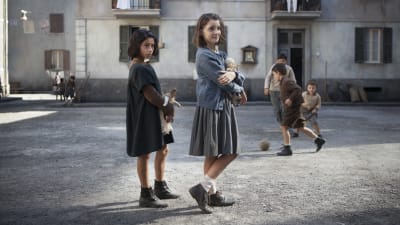 Lila (Ludovica Nasti) och Elena (Elisa Del Genio) står bredvid varandra på gatan och håller i varsin docka.
