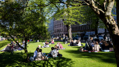 Människor sitter i en park i Helsingfors och njuter av solen.