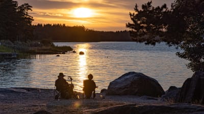 Två personer sitter på en strand under en solnedgång.