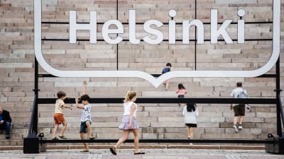 Människor står framför en Helsingforsskylt vid en trappa.