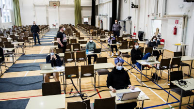 Studerande sitter i en gympasal och skriver studentprov.