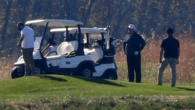 Donald Trump i vit keps står på en golfbana bredvid en golfbil.