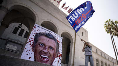 En demonstrant viftade med en kampanjflagga för återval av Trump utanför stadshuset i Los Angeles. Nidbilder på Kaliforniens guvernör Gavin Newsom förekom vid alla demonstrationer i Kalifornien på fredagen. 