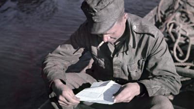 En soldat läser ett brev sittande i en båt.