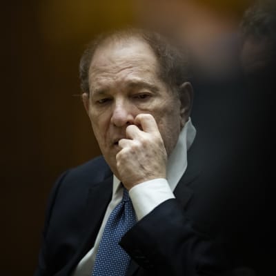 Harvey Weinstein kliar sig i ansiktet medan han tittar ner. Han sitter i en rättssal.