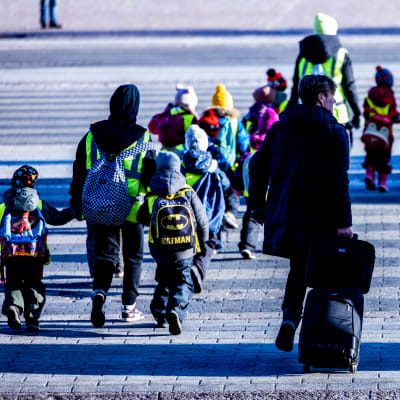 Lärare inom småbarnspedagogiken går hand i hand med barn när de korsar gatan på ett övergångsställe.