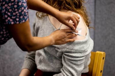 En vaccinerare pressar en pappersbit mot en persons axel som just blivit vaccinerad.